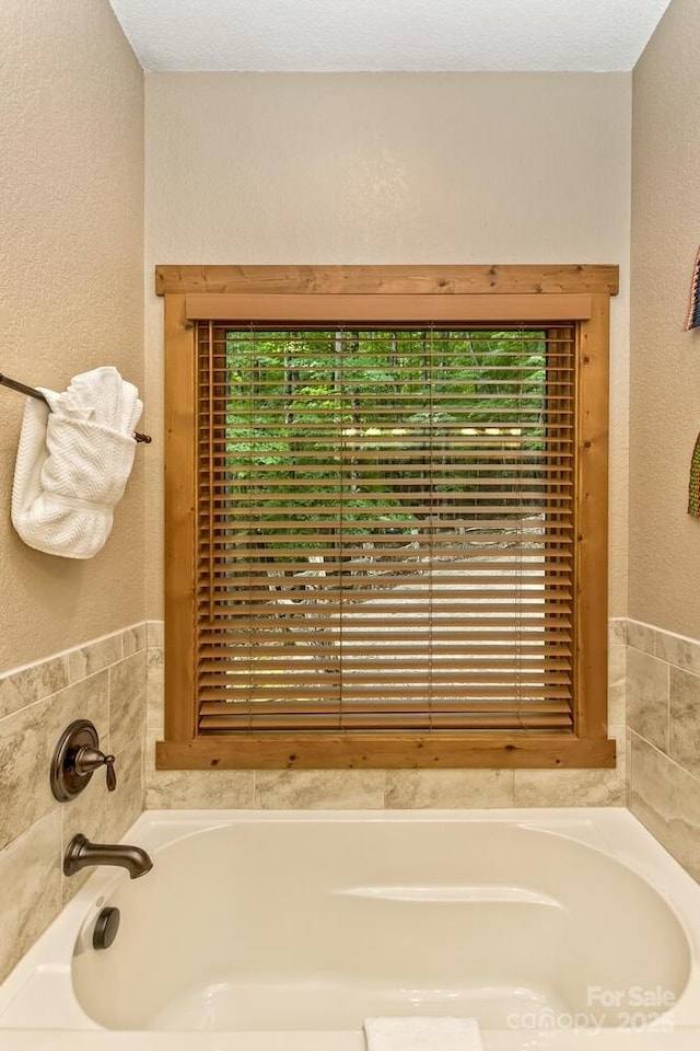 bathroom with a garden tub, a textured wall, and a healthy amount of sunlight