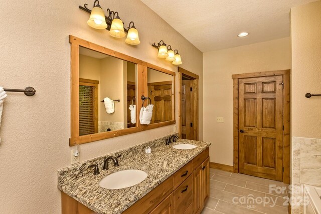 full bathroom featuring a sink, a textured wall, double vanity, and tile patterned floors