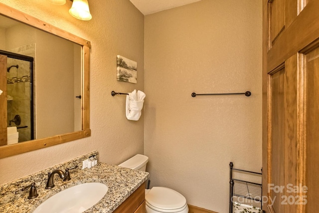 bathroom with a tile shower, toilet, vanity, and a textured wall