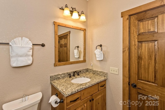 bathroom with toilet, vanity, and a textured wall