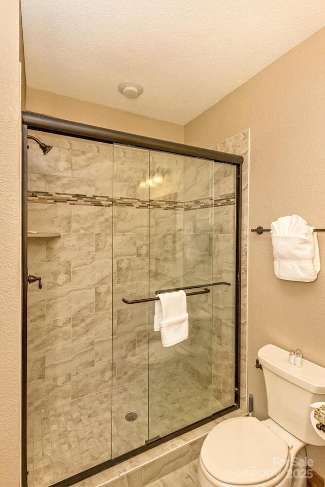 full bathroom with a textured wall, toilet, a stall shower, and a textured ceiling