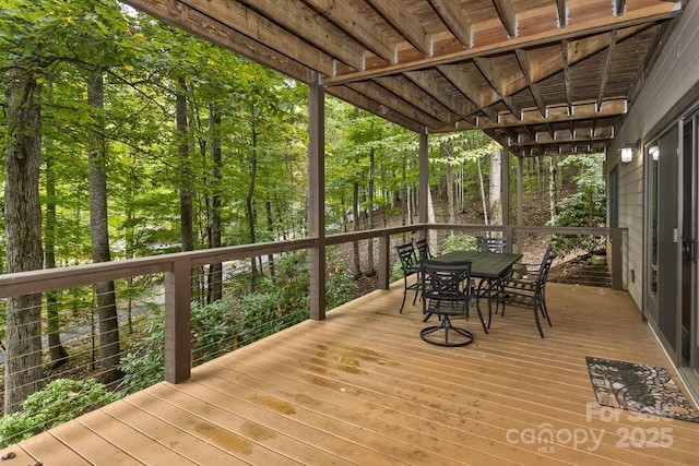 wooden terrace with outdoor dining area and a view of trees