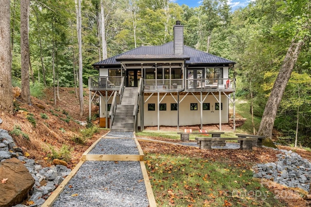 back of property featuring a wooded view, a wooden deck, stairs, a chimney, and metal roof