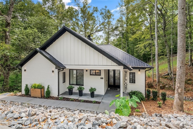 view of front of house with a porch, brick siding, and metal roof