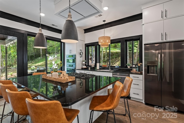 kitchen featuring visible vents, pendant lighting, a breakfast bar, stainless steel appliances, and white cabinetry