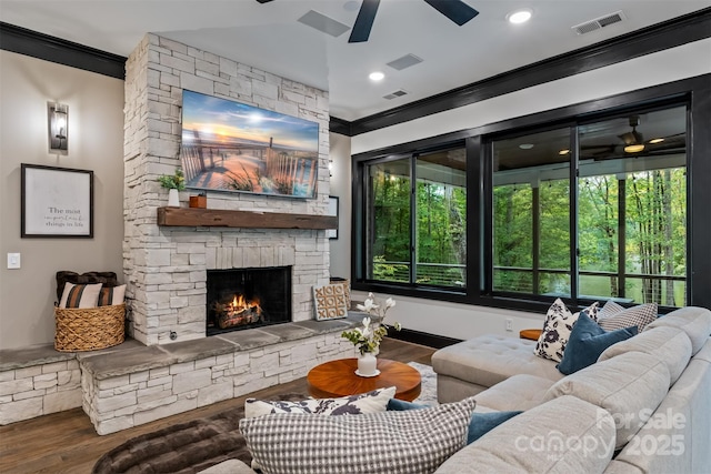 living area with a stone fireplace, wood finished floors, visible vents, and ornamental molding