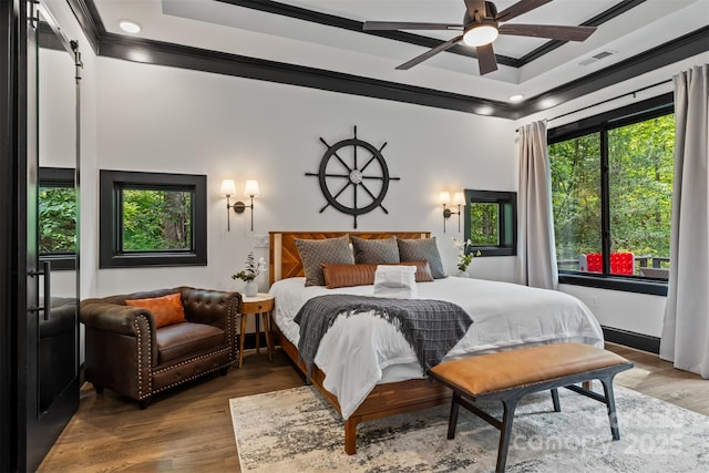 bedroom featuring a barn door, wood finished floors, visible vents, and ornamental molding