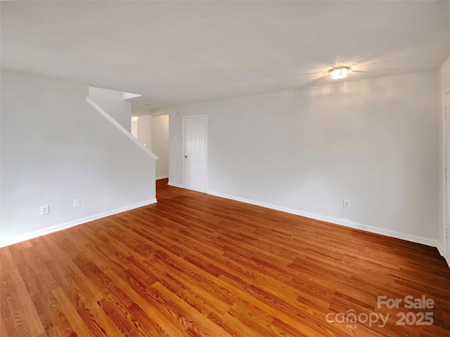 empty room with stairs, wood finished floors, and baseboards