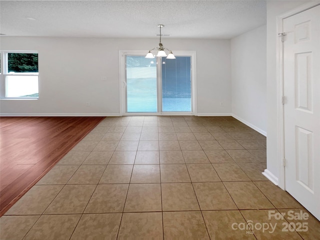 spare room featuring baseboards, a textured ceiling, a chandelier, and tile patterned flooring