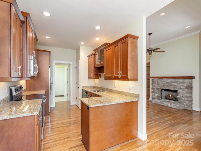 kitchen with brown cabinetry, stainless steel appliances, light stone counters, and a sink