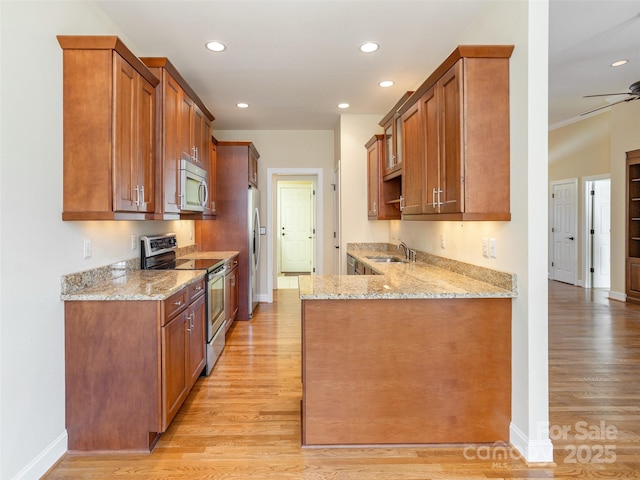 kitchen with a sink, light stone counters, light wood finished floors, and stainless steel appliances