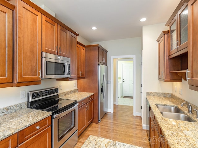 kitchen with light wood-type flooring, light stone counters, recessed lighting, stainless steel appliances, and a sink