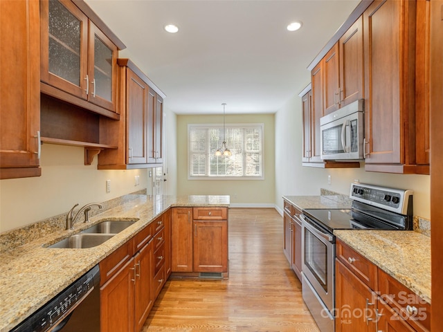 kitchen featuring light wood finished floors, glass insert cabinets, appliances with stainless steel finishes, a peninsula, and a sink