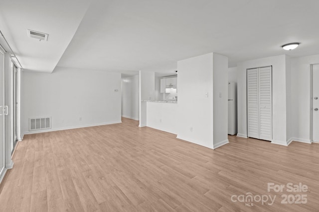 unfurnished living room with baseboards, visible vents, and light wood-type flooring