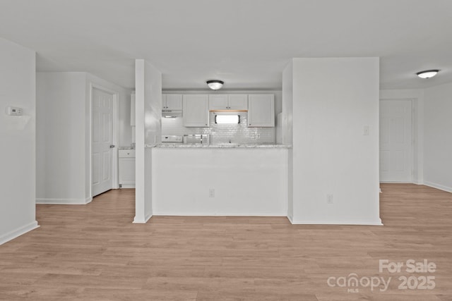 kitchen with white microwave, backsplash, baseboards, light wood-style flooring, and white cabinets