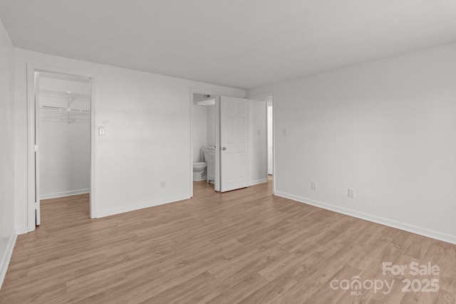 unfurnished bedroom with a spacious closet, light wood-style floors, and baseboards