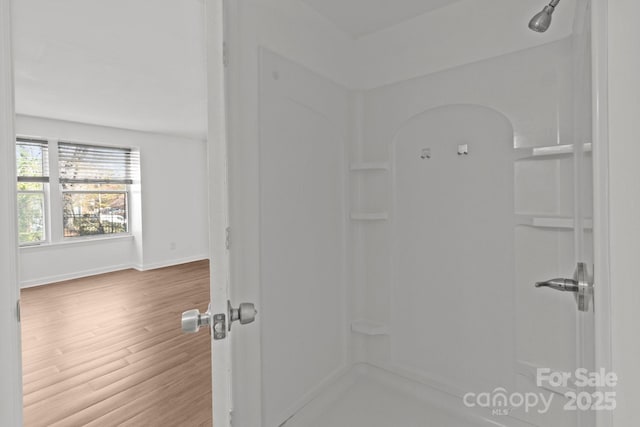 full bathroom with wood finished floors, a shower, and baseboards