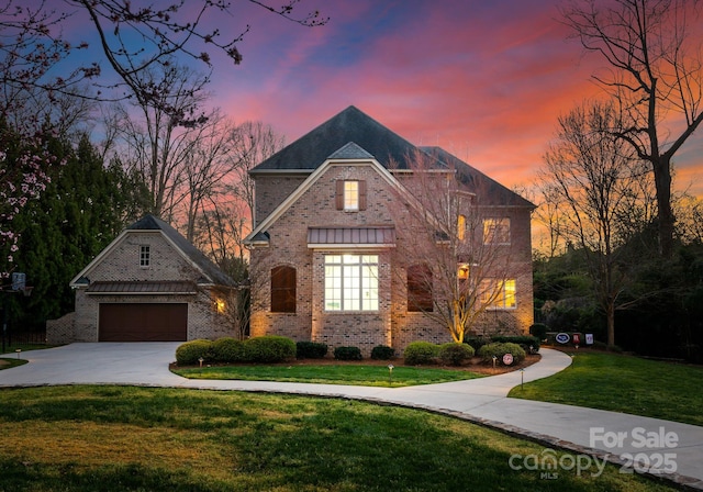 french country inspired facade featuring brick siding, a garage, concrete driveway, and a front yard