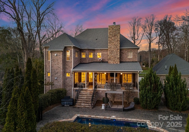 back of property with an outdoor pool, a patio, stairs, and a chimney