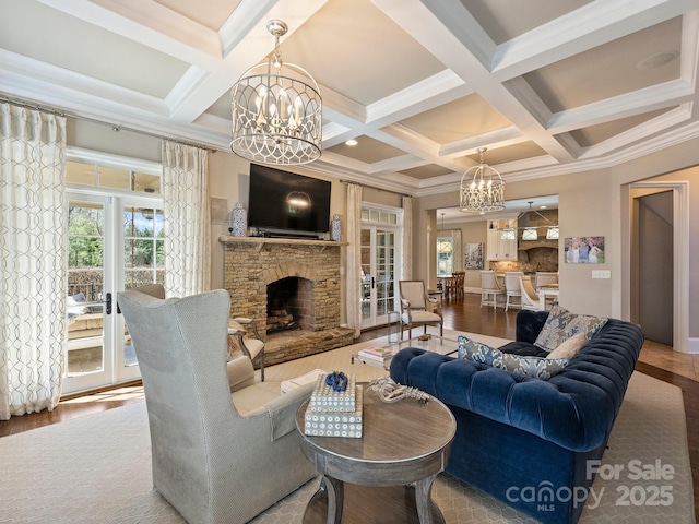 living area featuring beam ceiling, a notable chandelier, a stone fireplace, and wood finished floors