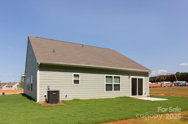 rear view of house featuring central AC unit, a lawn, and roof with shingles