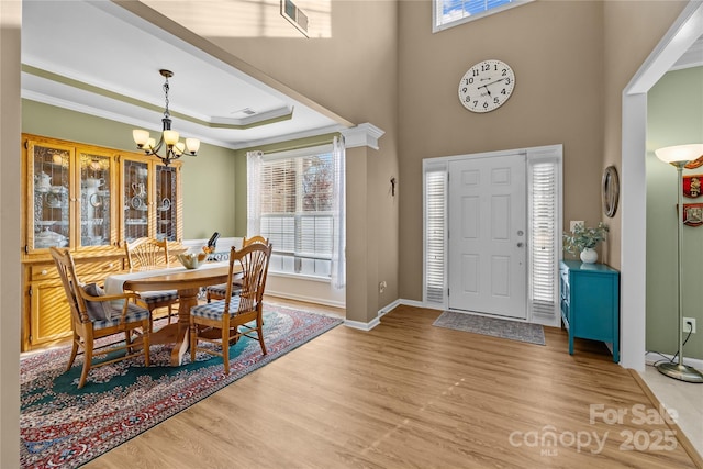 entryway featuring baseboards, an inviting chandelier, a tray ceiling, ornamental molding, and light wood-style floors