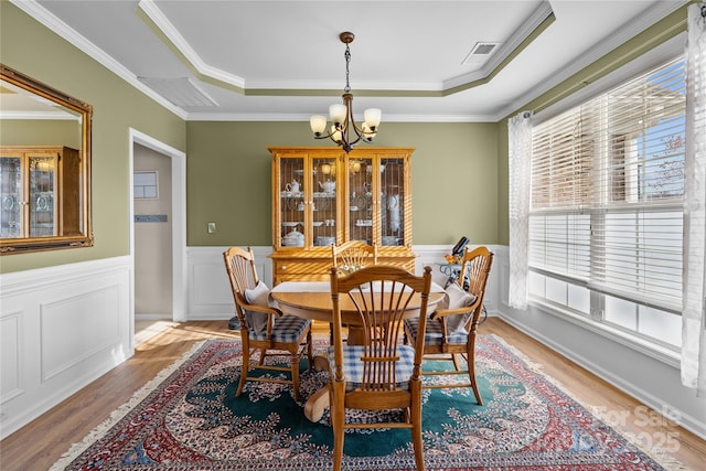 dining space featuring visible vents, light wood-style floors, wainscoting, a raised ceiling, and a notable chandelier