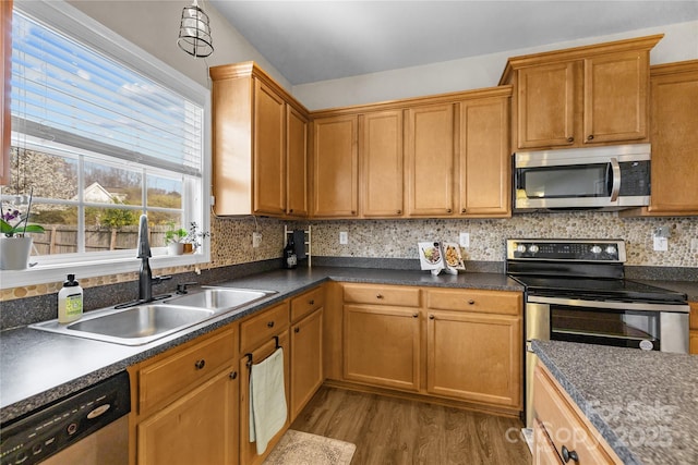 kitchen featuring wood finished floors, a sink, decorative backsplash, appliances with stainless steel finishes, and dark countertops