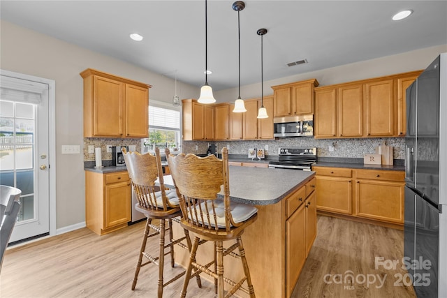 kitchen featuring tasteful backsplash, a center island, light wood-type flooring, and stainless steel appliances