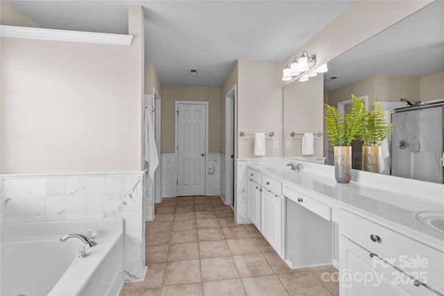 bathroom featuring a wainscoted wall, double vanity, a stall shower, a bath, and a sink