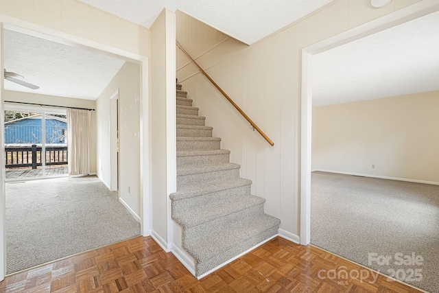 stairway with ceiling fan, carpet flooring, baseboards, and a textured ceiling