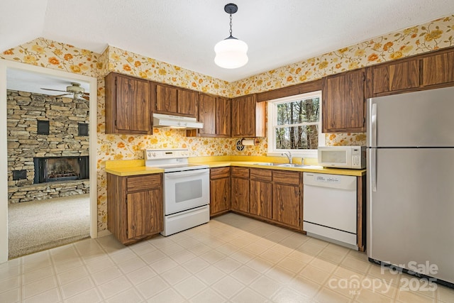 kitchen featuring under cabinet range hood, white appliances, wallpapered walls, and a sink