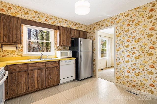 kitchen featuring white appliances, visible vents, wallpapered walls, a sink, and light countertops