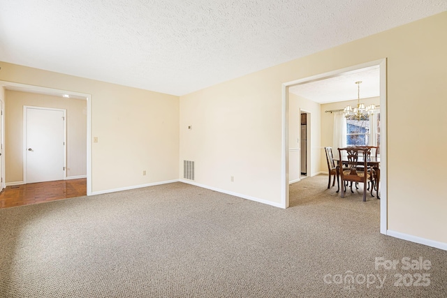 unfurnished room with visible vents, a textured ceiling, carpet flooring, baseboards, and a chandelier