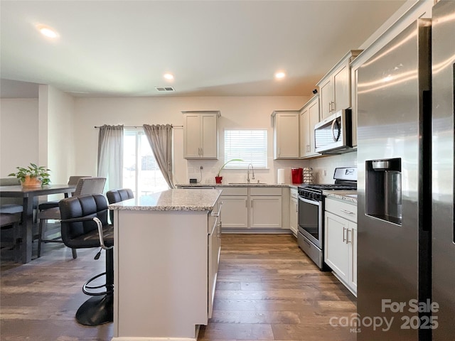 kitchen with visible vents, a center island, appliances with stainless steel finishes, dark wood-style floors, and a sink