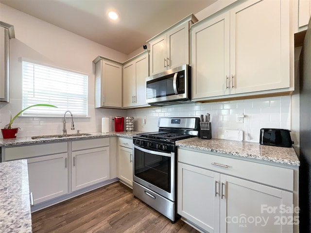 kitchen featuring a sink, light stone counters, dark wood-style floors, appliances with stainless steel finishes, and decorative backsplash