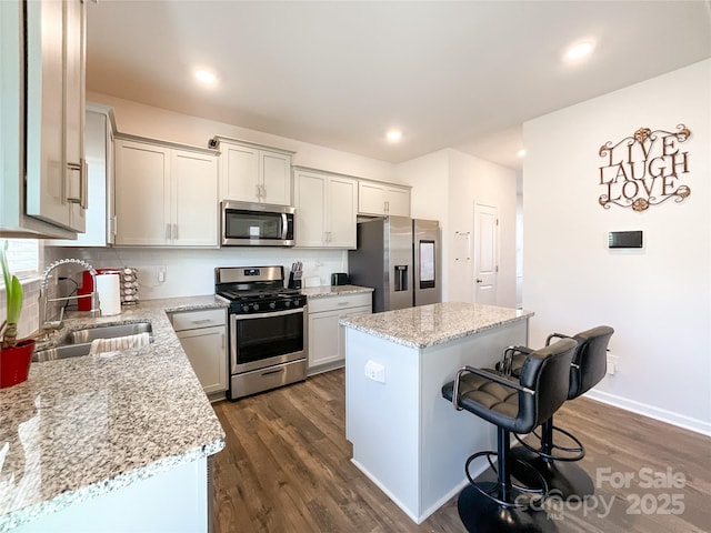 kitchen with a sink, a kitchen island, stainless steel appliances, a breakfast bar area, and dark wood-style flooring