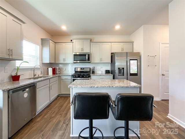 kitchen featuring backsplash, a center island, appliances with stainless steel finishes, wood finished floors, and a sink