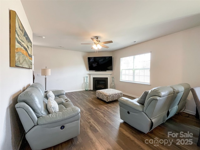 living area with visible vents, a glass covered fireplace, baseboards, ceiling fan, and dark wood-style flooring