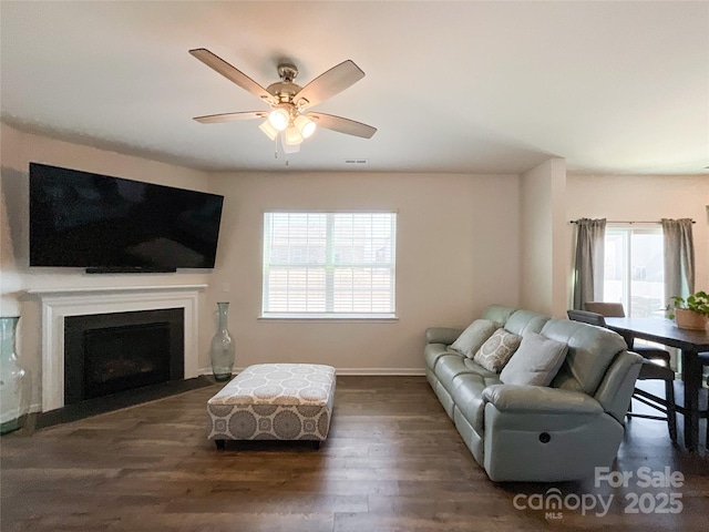 living area with visible vents, baseboards, a fireplace with flush hearth, wood finished floors, and a ceiling fan