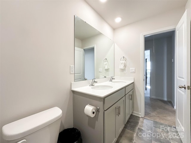 bathroom with double vanity, toilet, baseboards, and a sink