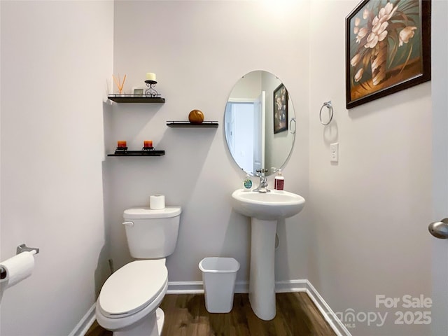 half bathroom with toilet, wood finished floors, baseboards, and a sink