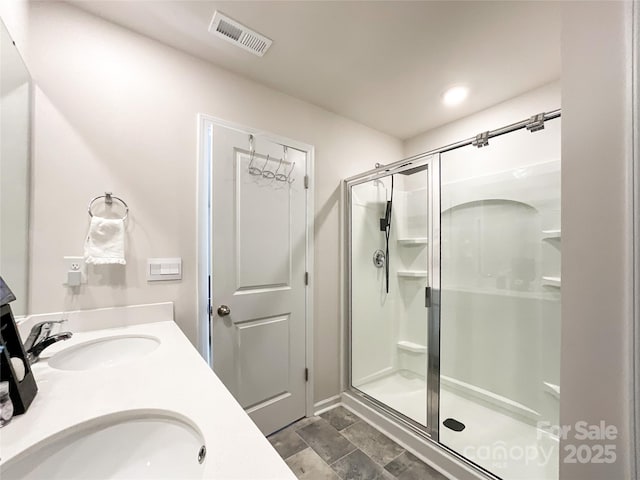 full bath with a shower stall, double vanity, visible vents, and a sink