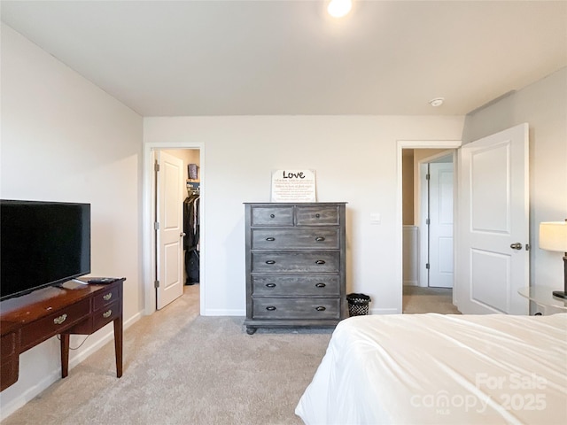 bedroom featuring a walk in closet, baseboards, light colored carpet, and a closet