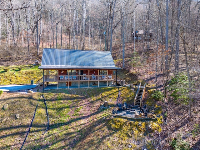 view of front of house featuring a fire pit, a forest view, stairway, a wooden deck, and metal roof