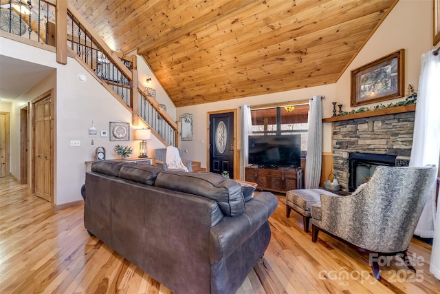 living area featuring stairs, a stone fireplace, wood ceiling, and light wood-type flooring