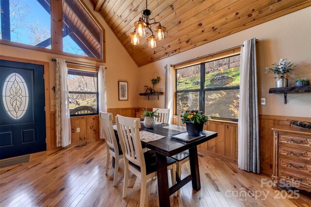 dining space with an inviting chandelier, wood ceiling, a wainscoted wall, and light wood-type flooring