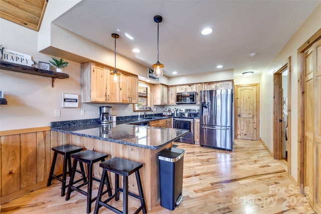 kitchen with light wood finished floors, appliances with stainless steel finishes, dark stone counters, and a peninsula