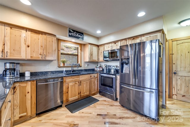 kitchen with dark stone counters, recessed lighting, a sink, appliances with stainless steel finishes, and light wood-type flooring