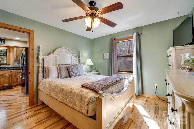 bedroom with baseboards, ceiling fan, light wood-style flooring, ensuite bathroom, and freestanding refrigerator